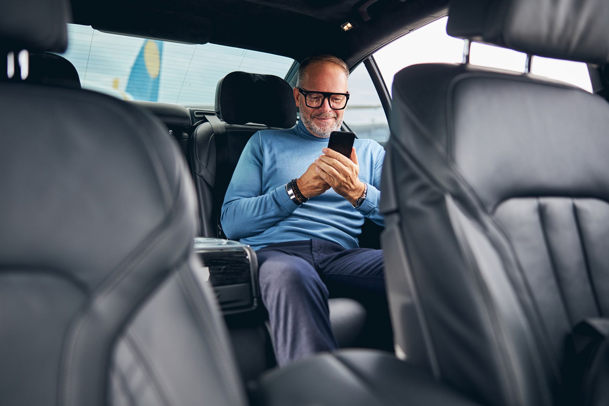 Bearded Caucasian male entrepreneur with a pleased smile reading a text message in the taxicab